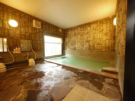 Um spa com paredes de pedra, banheira de hidromassagem, piso de pedra e uma janela que permite entrada de luz natural.