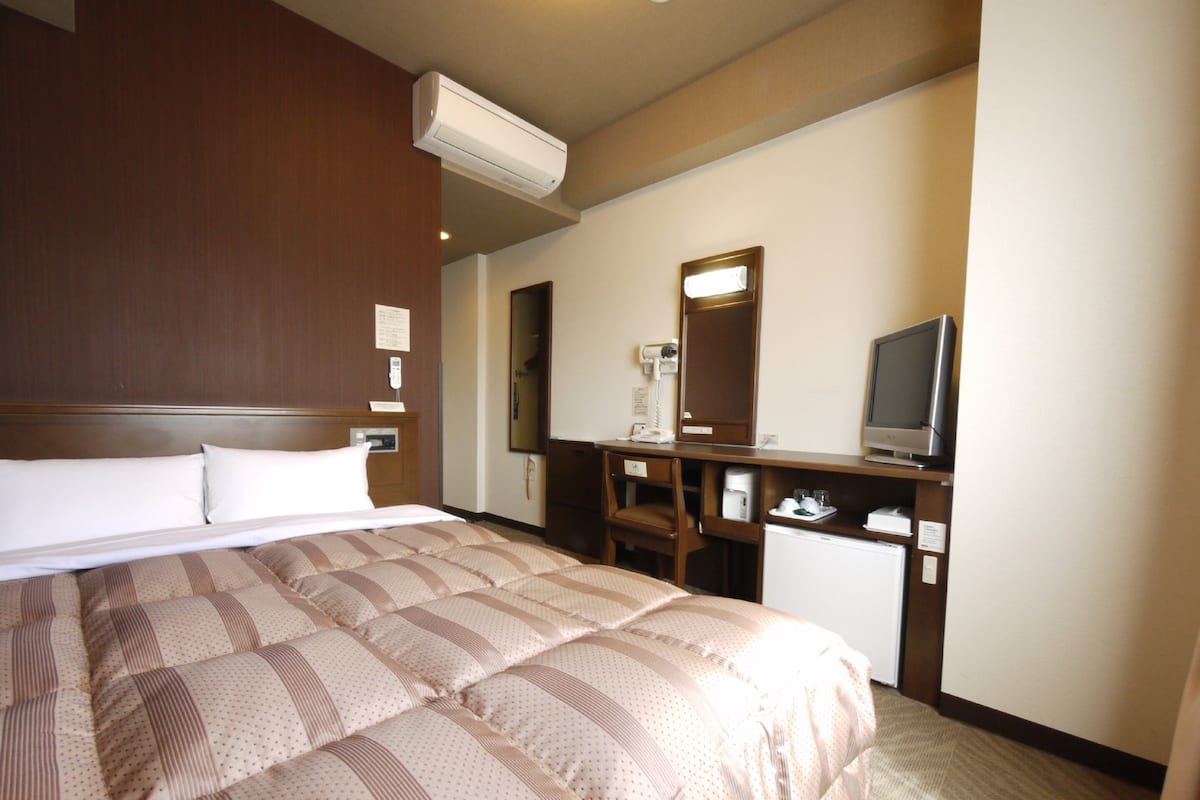 A hotel room with a large bed, a desk with a television, and a mirror.