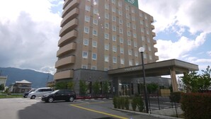 Un hotel de varios pisos con un letrero llamativo en la parte superior, un acceso cubierto y un estacionamiento con coches.