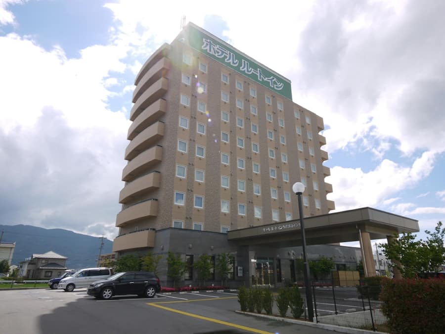 A multi-story hotel with a prominent sign at the top, a covered entrance, and a parking area with cars.