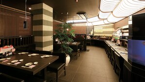 En restaurang med avskilda bås och bord, en krukväxt och ett köksområde i bakgrunden.