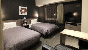 Ett hotellrum med två sängar, ett skrivbord, en tv, ett nattduksbord och ett konstverk som hänger på väggen.