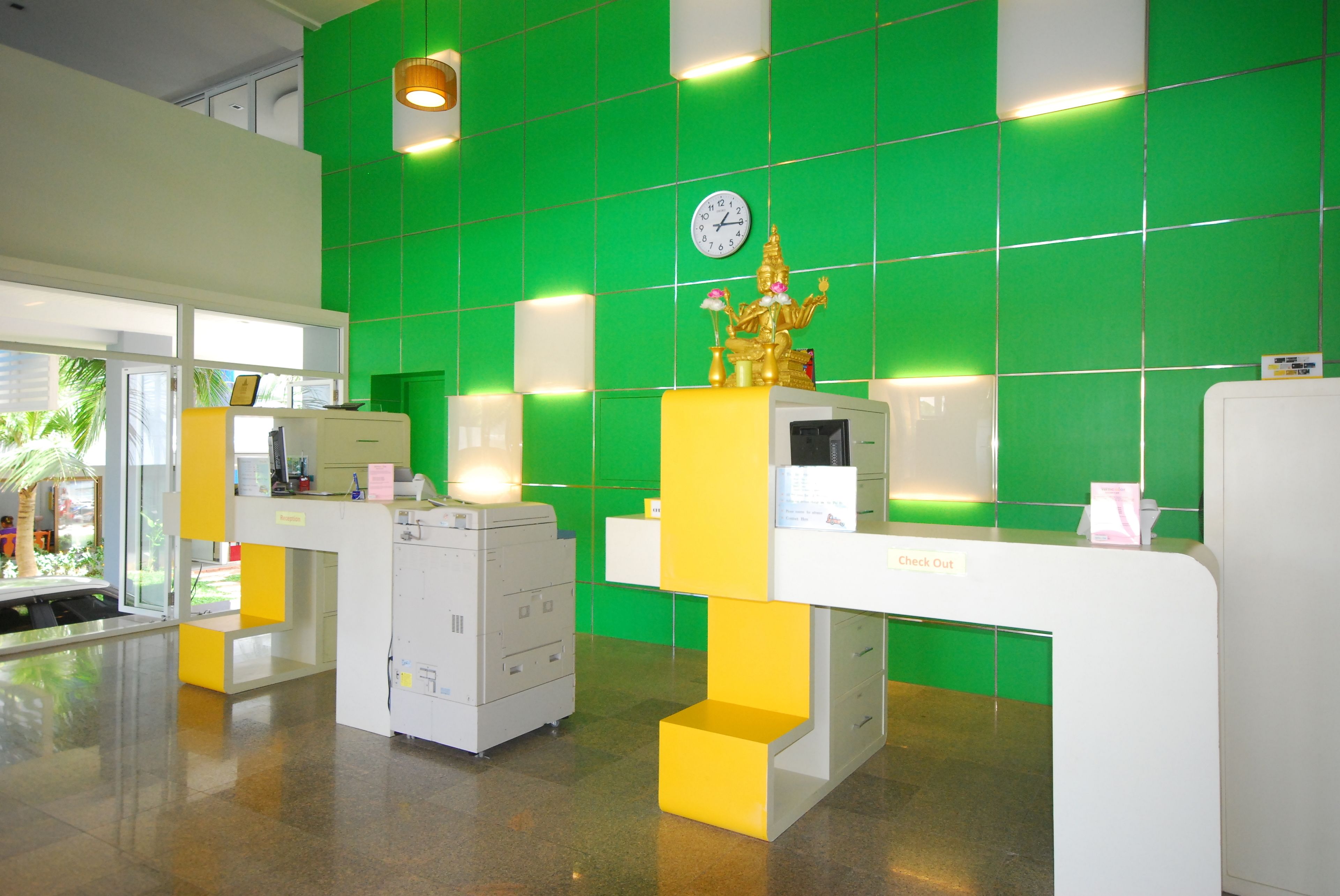 Zona de recepción con pared de azulejos verdes, un reloj y una estatua.