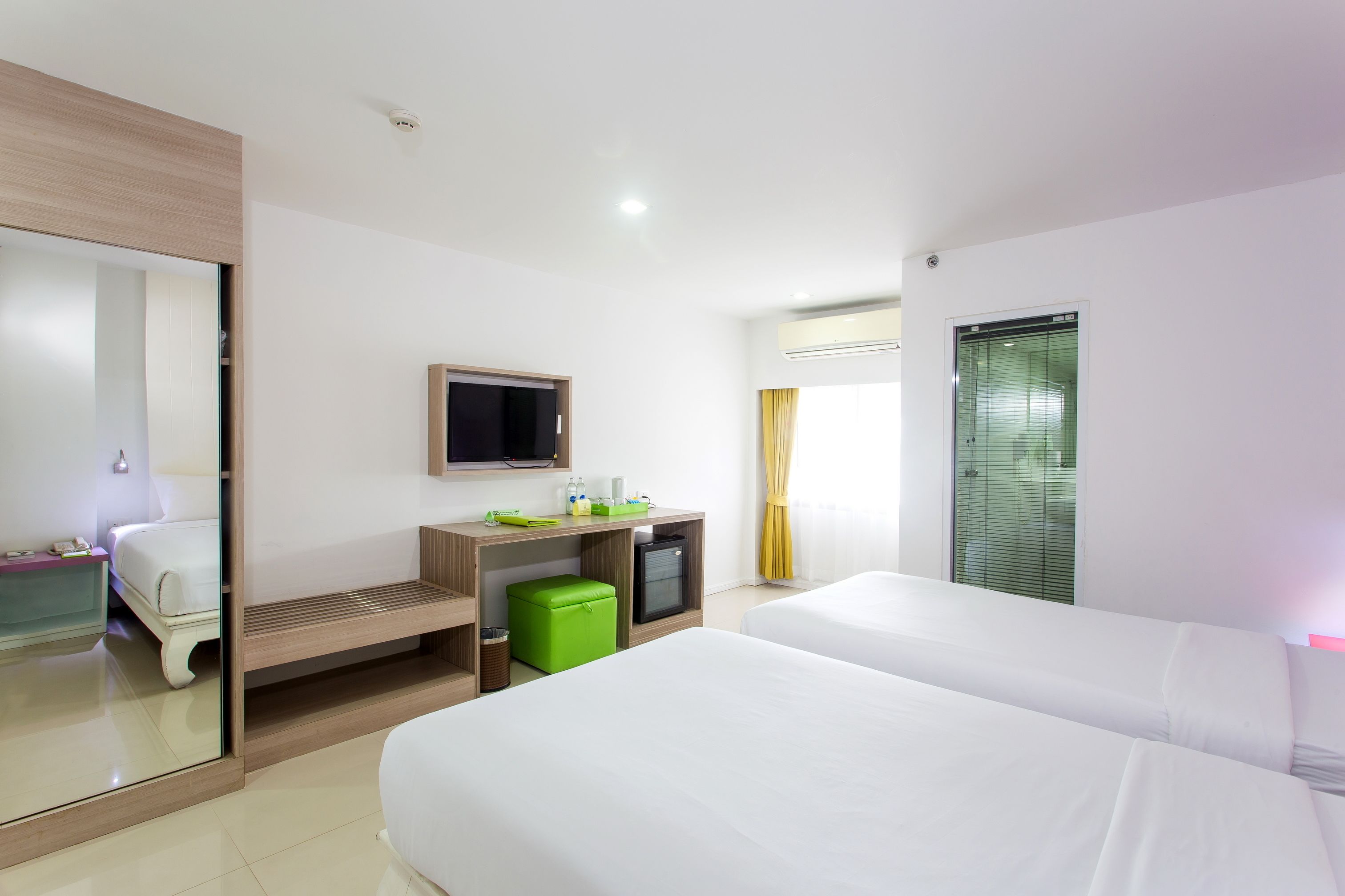 Une chambre d’hôtel avec deux lits, un bureau avec un ordinateur, une télévision et une fenêtre avec des rideaux.