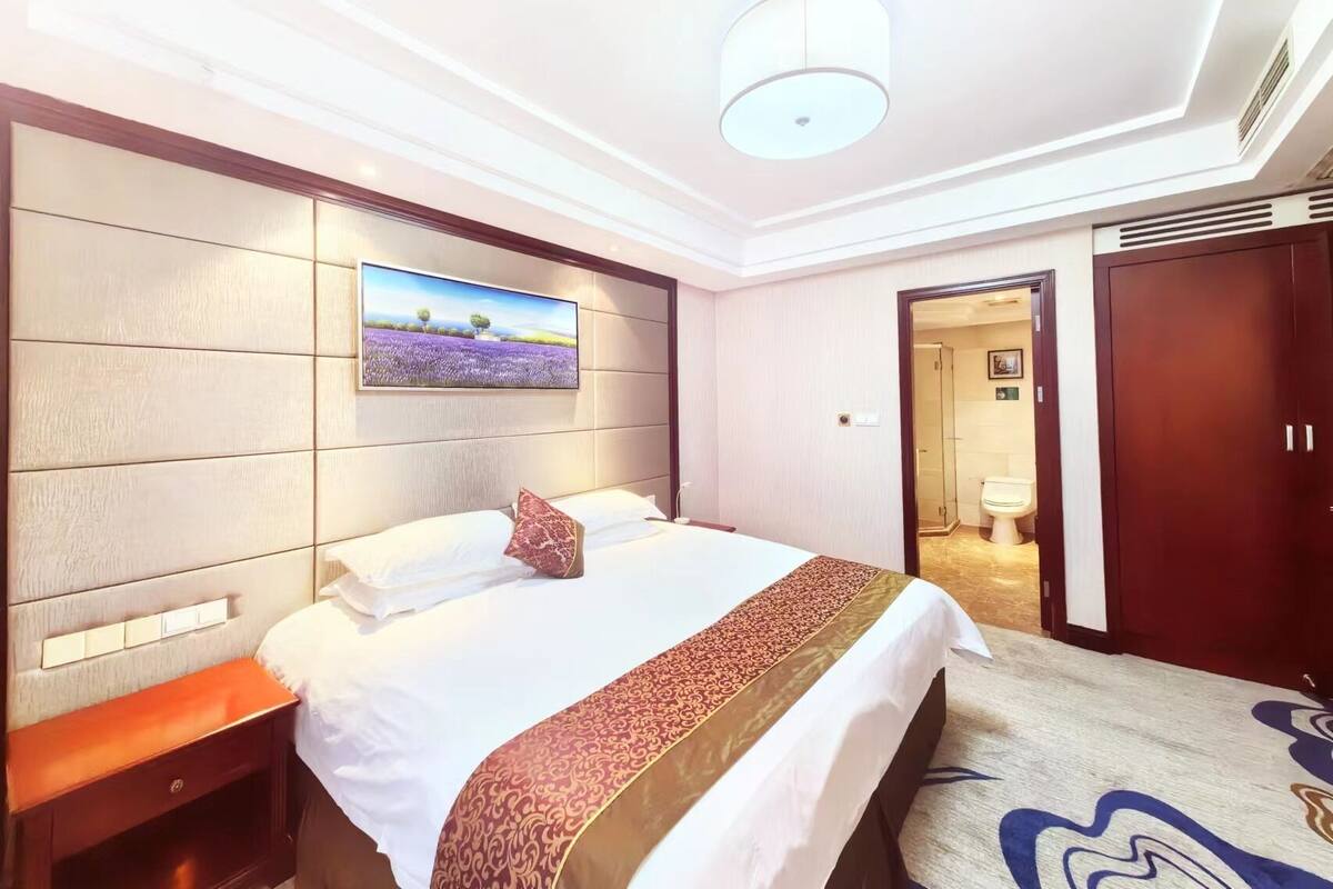 Een hotelkamer met een groot bed, een nachtkastje, een aan de muur bevestigde televisie en een deur naar een badkamer.
