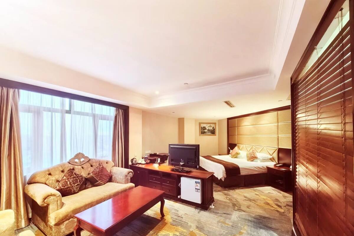 Een hotelkamer met een bank, een salontafel, een televisie, een bed met hoofdeinde en een vloerbedekking.