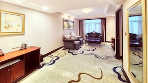 A hotel room with a sofa, armchair, and a wooden cabinet.