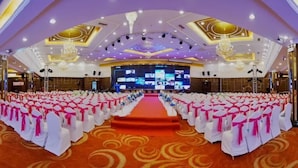 A large hall with rows of white chairs with pink sashes, a central stage, and a large screen at the front.