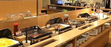 A buffet setup with various food stations, including a hot sauce dispenser, a coffee machine, and a refrigerator.