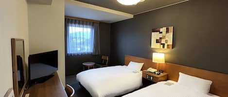 A hotel room with two beds, a desk, a chair, a lamp, a phone, and a window with curtains.
