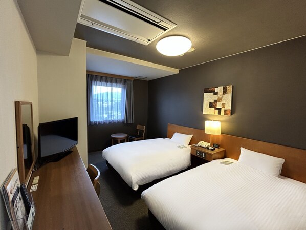 Habitación de hotel con dos camas, un escritorio, una silla, una lámpara, un teléfono y una ventana con cortinas.