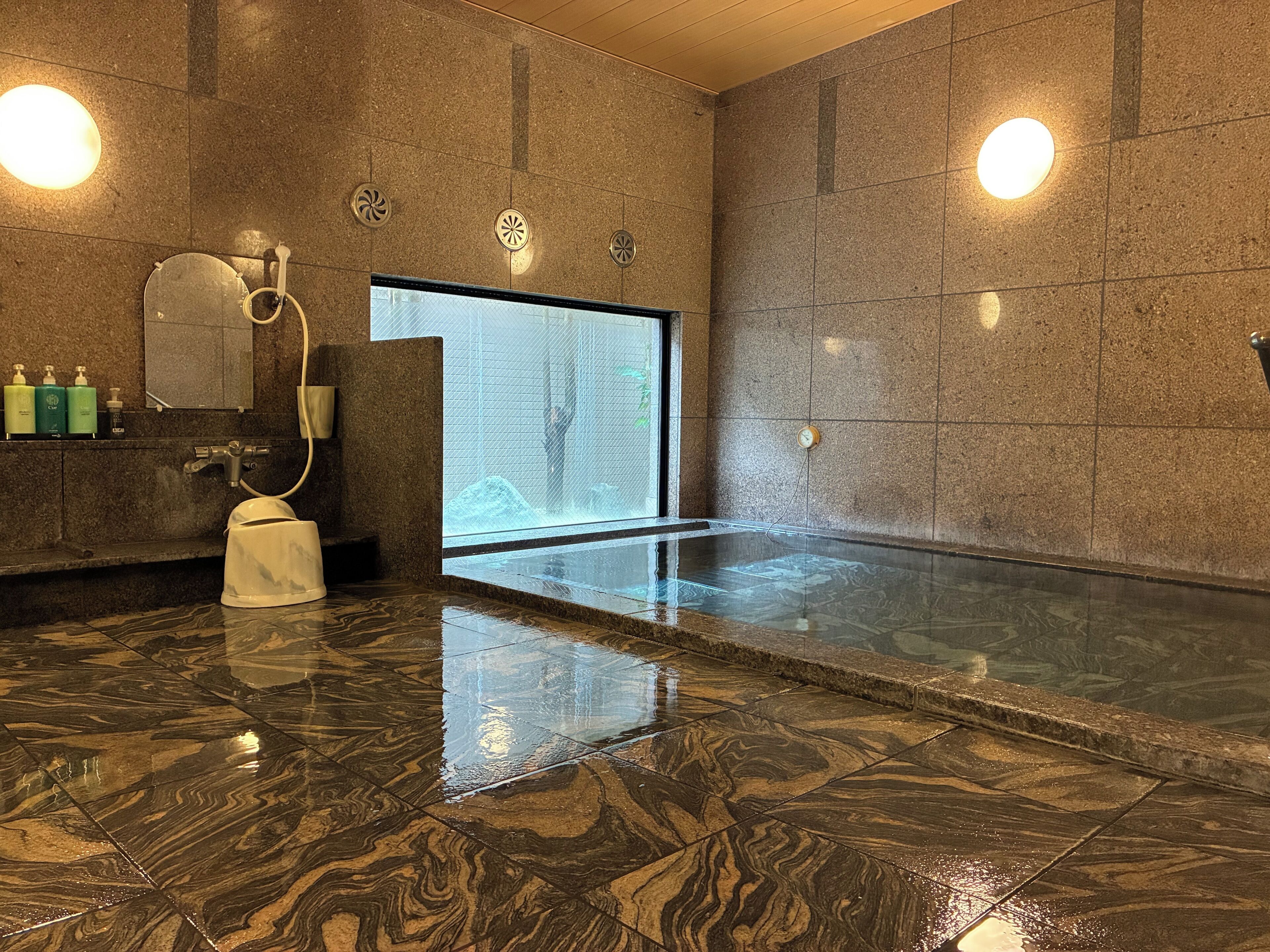 Un baño moderno con suelo de mármol, ducha con cerramiento de vidrio y lavamanos blanco.