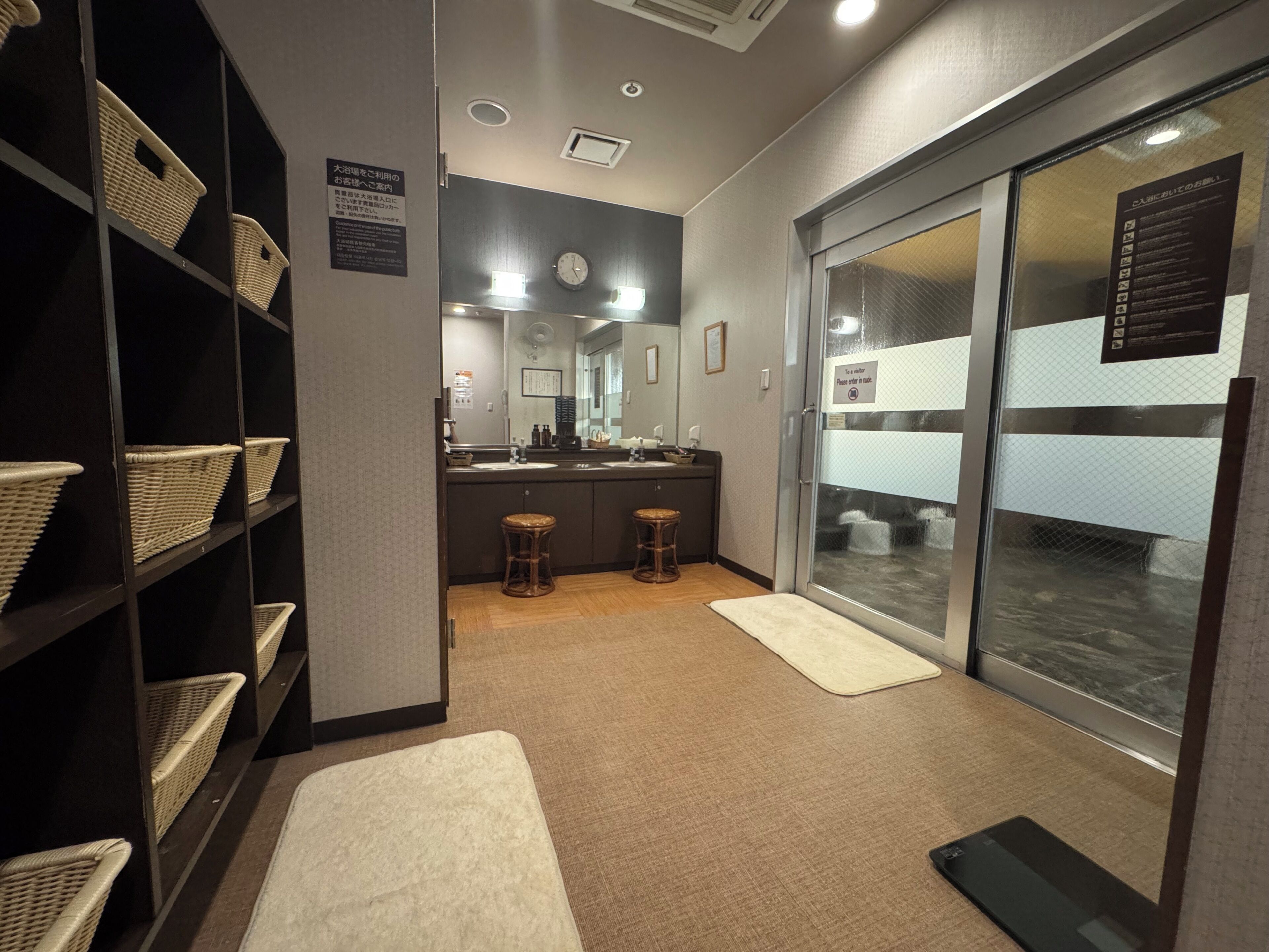 A hotel room with a large window, a mirror, a sink, and wicker baskets on shelves.