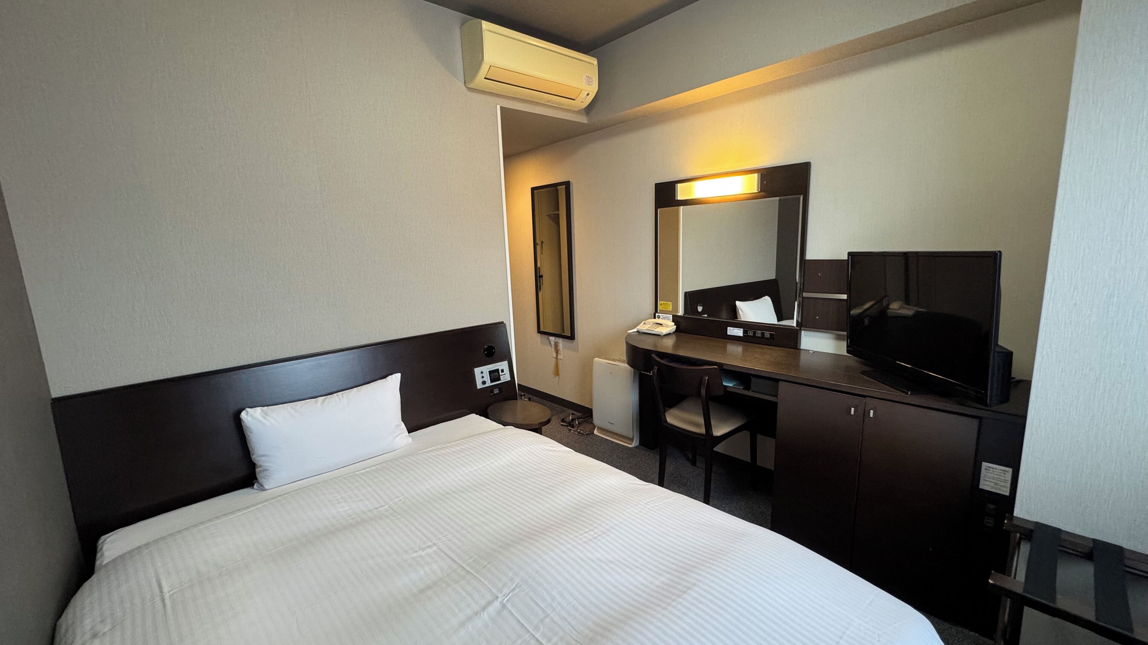 Une chambre d’hôtel équipée d’un lit, d’un bureau, d’une chaise, d’une télévision et d’un miroir.
