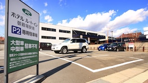 Señal de hotel con texto en japonés, estacionamiento con varios autos y un edificio al fondo.