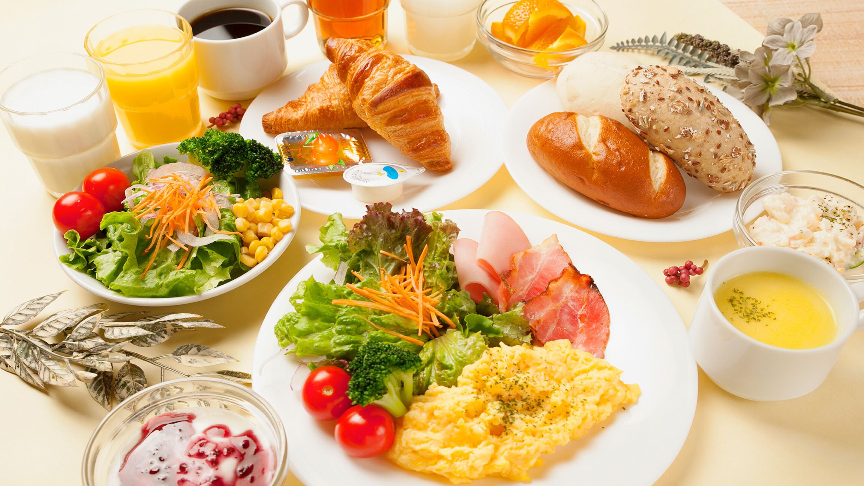 Un desayuno con cruasanes, huevos, verduras y bebidas.