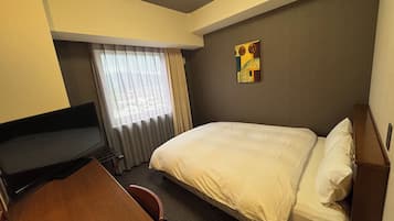 A hotel room with a bed, a TV, a desk, and a window with curtains.