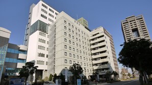 Ein mehrstöckiges Hotel mit modernem architektonischen Design, das einen markanten Eingangsbereich und einen Parkplatz vor dem Gebäude hat.