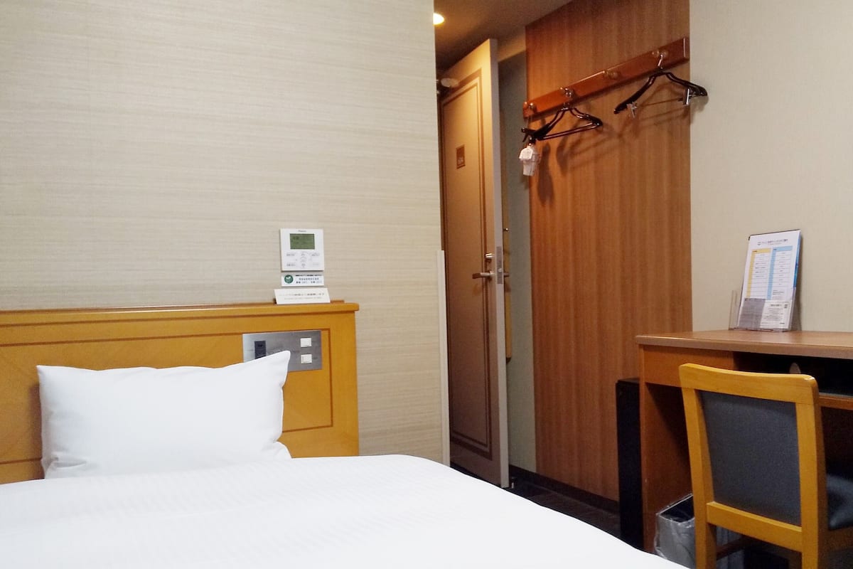 Ein Hotelzimmer mit Bett, Schreibtisch, Stuhl, Kleiderhaken und einer Tür.