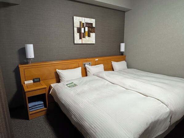 Habitación de hotel con una cama grande, dos mesitas de noche, una obra de arte en la pared y un pequeño estante con toallas dobladas.