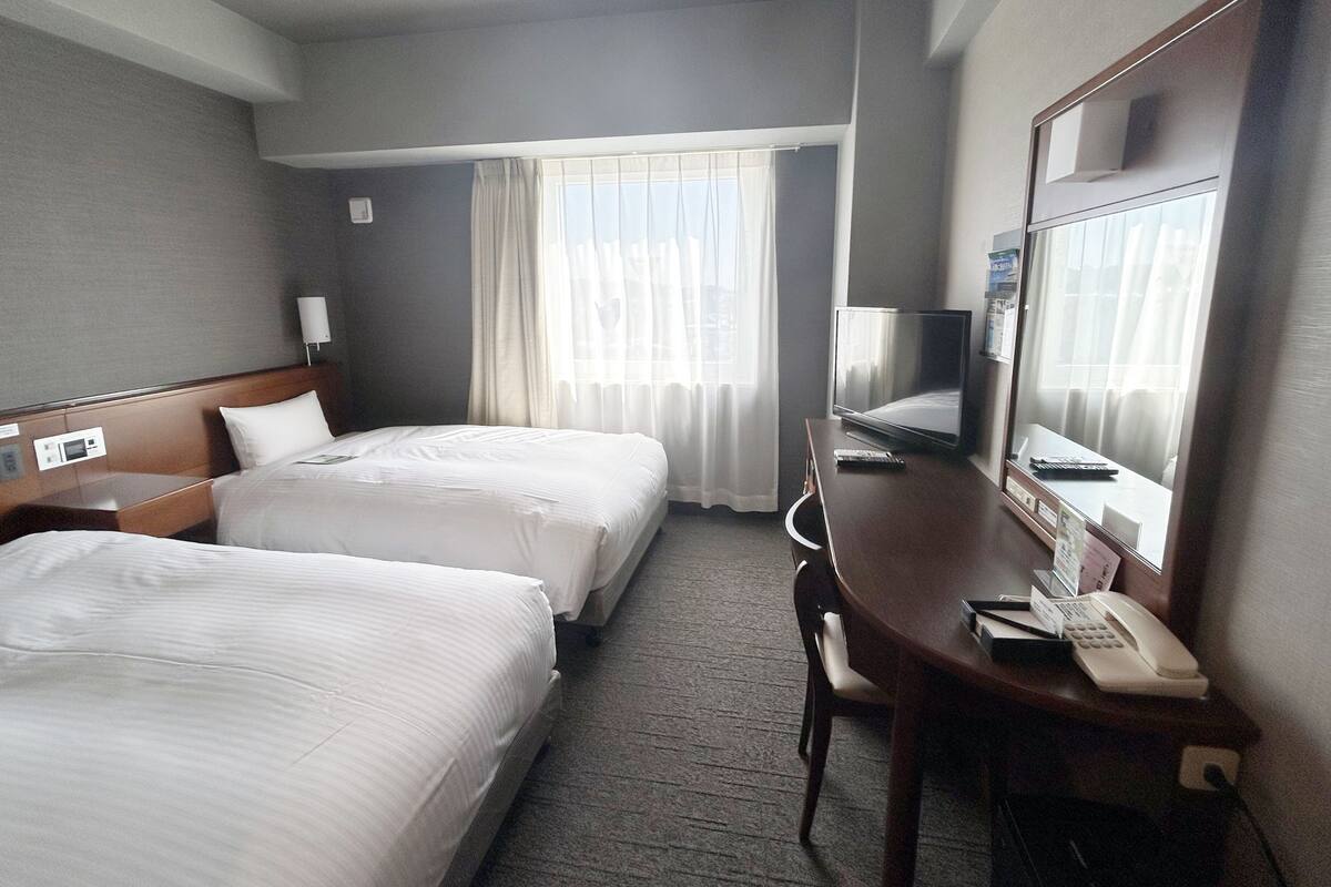 A hotel room with two beds, a desk with a telephone, a television, and a large mirror.