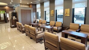 A hotel lobby with a modern design, featuring a seating area with sofas and armchairs, a reception desk, and large windows offering views of the outside. - Hotel Route Inn Iwata Inter (Iwata)