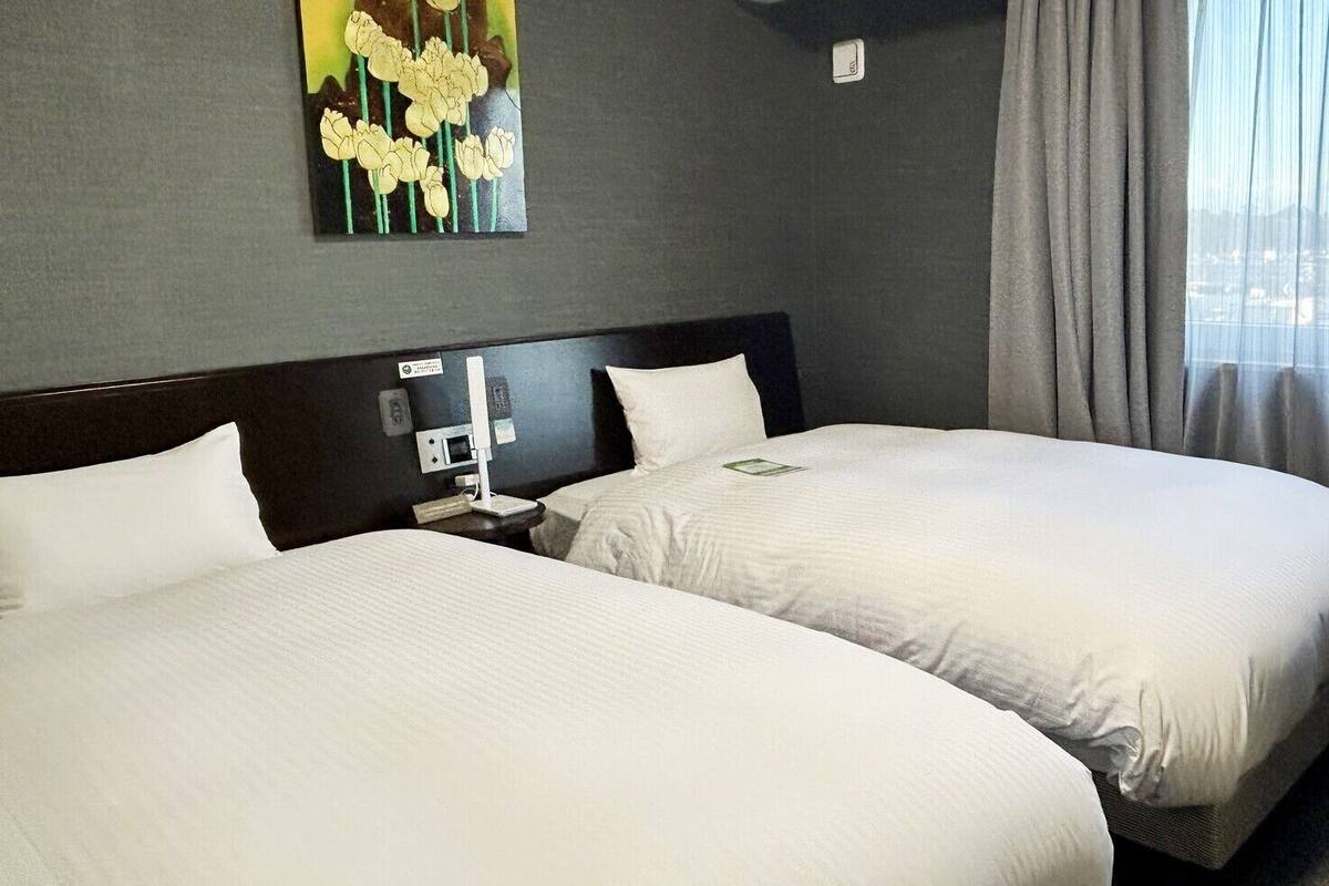 A hotel room with two beds, a nightstand, a painting, and a window with curtains.