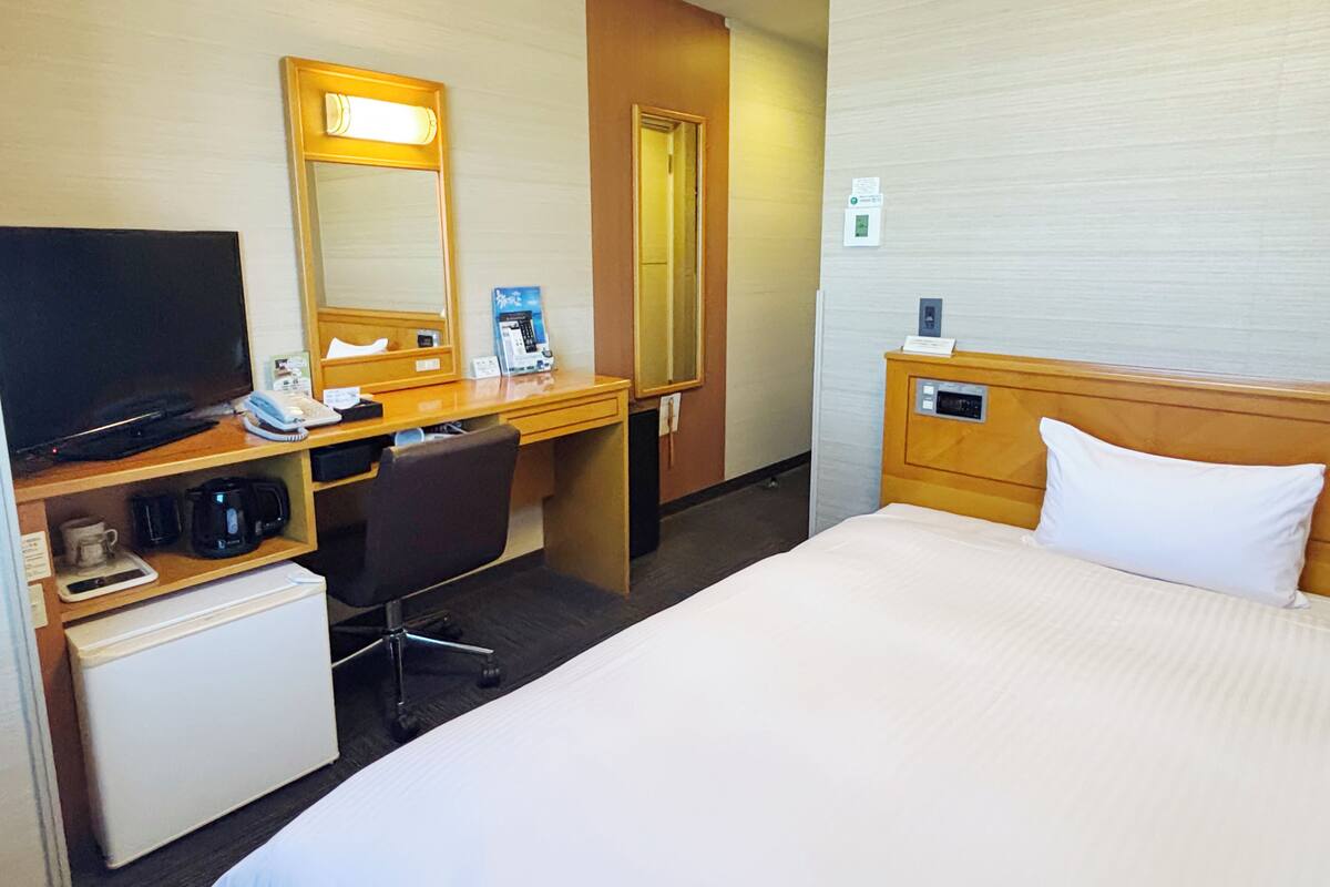 Quarto de hotel com cama, escrivaninha com computador, cafeteira, televisão e telefone.