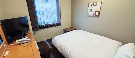 Habitación de hotel con cama, escritorio con televisor, ventana con cortinas y una obra de arte colgada en la pared.