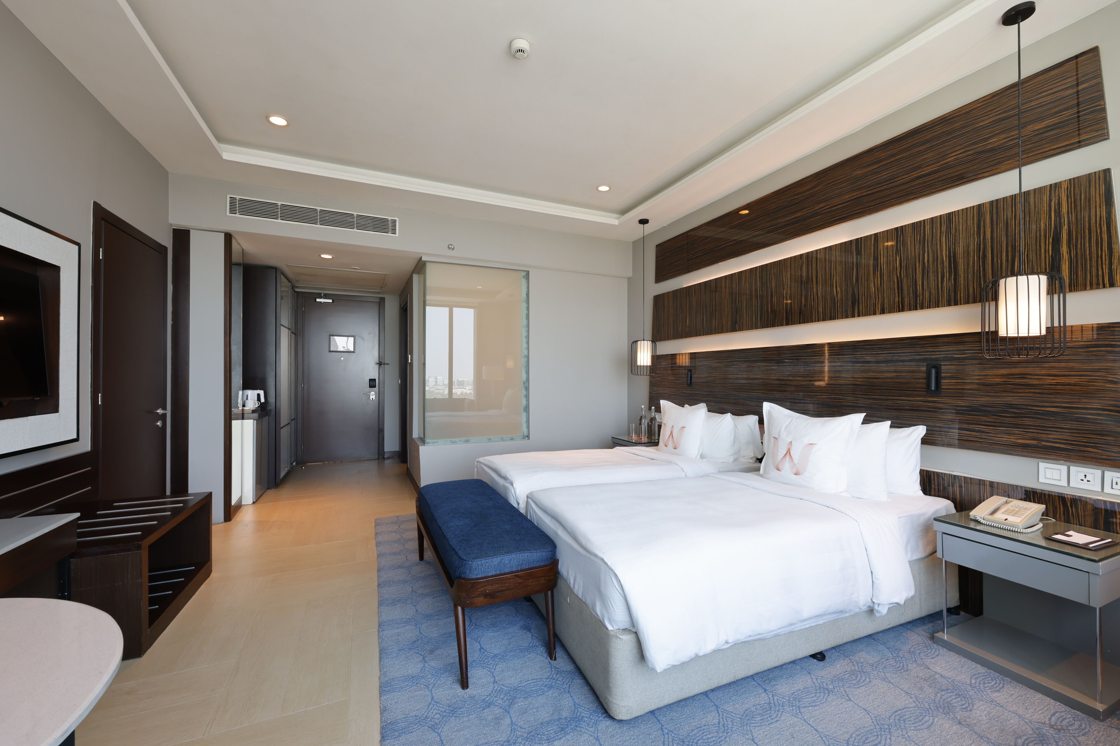 A modern hotel room with a large bed, a desk, a TV, and a bathroom visible through an open door.