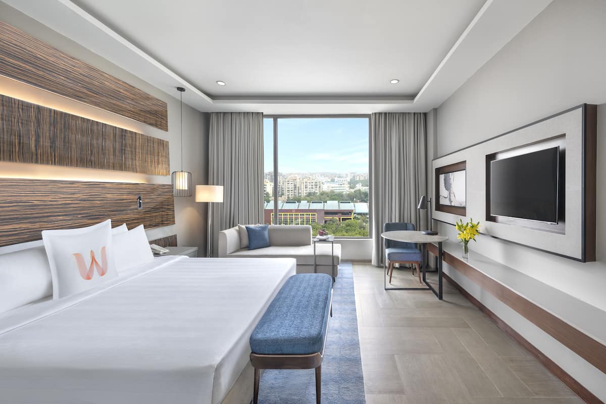 A hotel room with a large bed, a desk, a TV, and a view of the city.