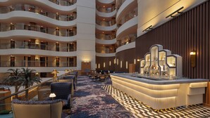 Un'ampia hall d'albergo su più livelli, con un bar centrale, zone salotto e una moquette decorata.