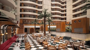 Un'ampia hall d'albergo su più livelli, con aree ristorazione, una scala e una zona piscina.