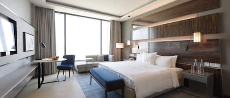 A modern hotel room with a large bed, a desk, a chair, and a TV.