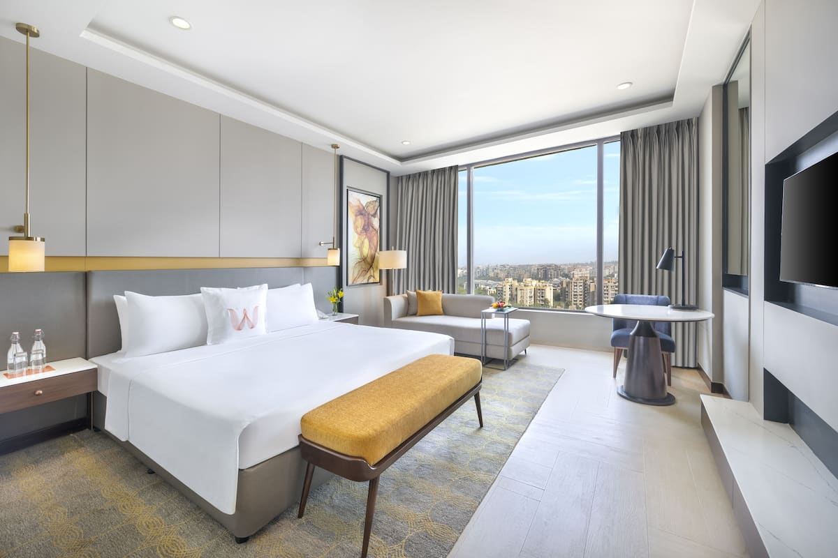 A modern hotel room with a large bed, a sofa, a small table, and a TV.