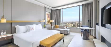 Una habitación de hotel moderna con una cama grande, un sofá, una mesita y un televisor.