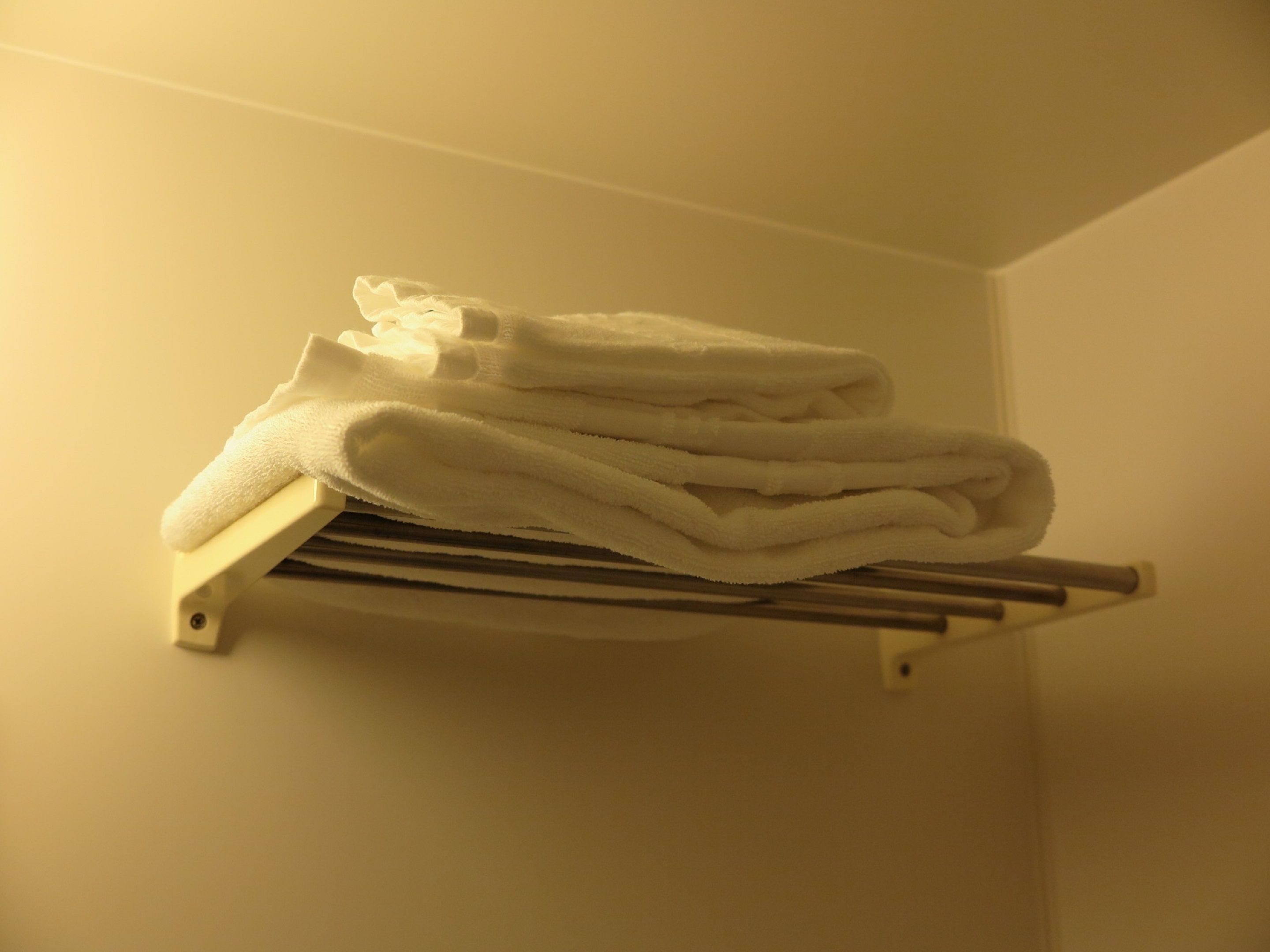 A stack of white towels on a metal towel rack in a room with plain walls.