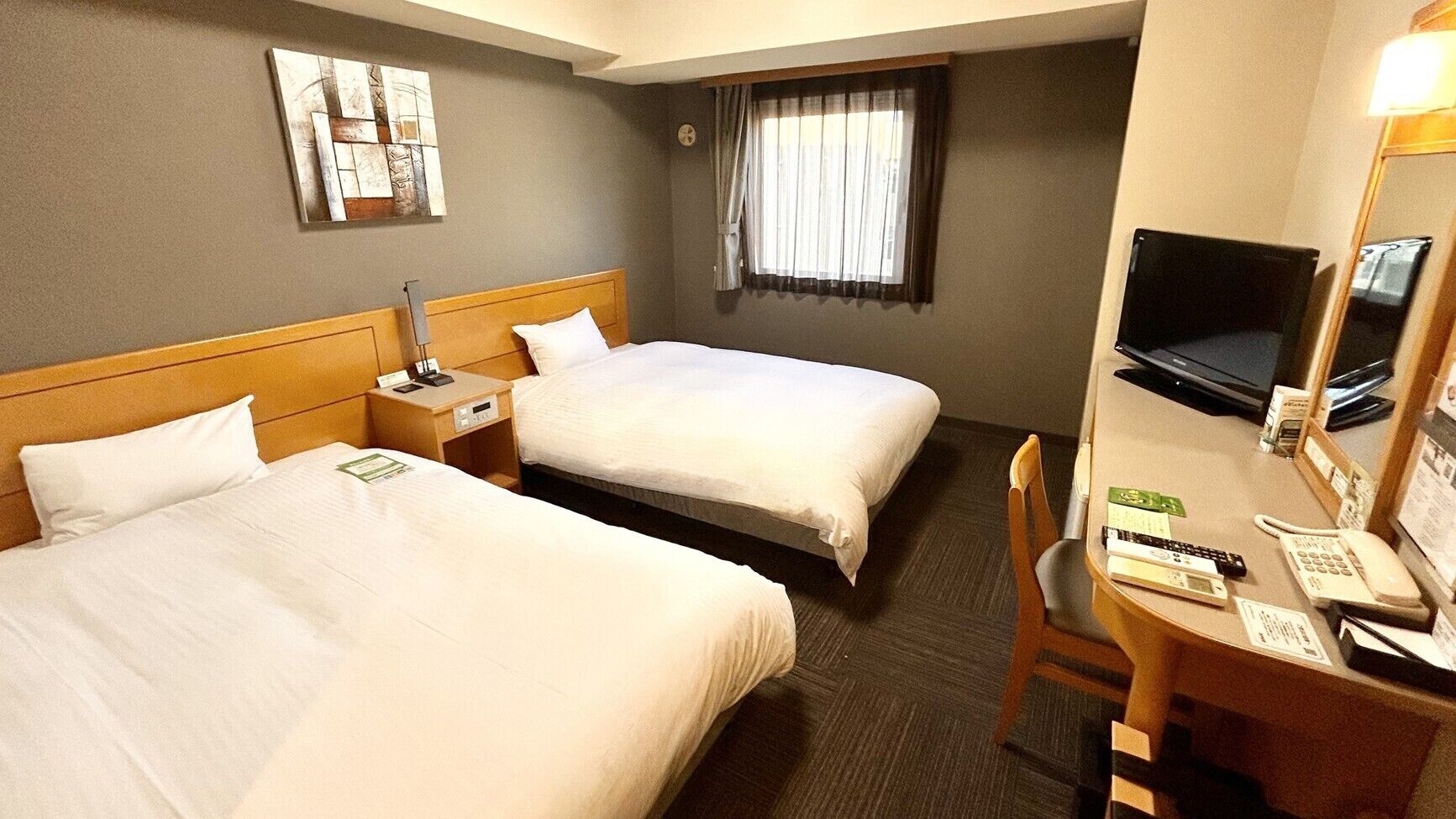 A hotel room with two beds, a desk with a chair, a television, and a window with curtains.