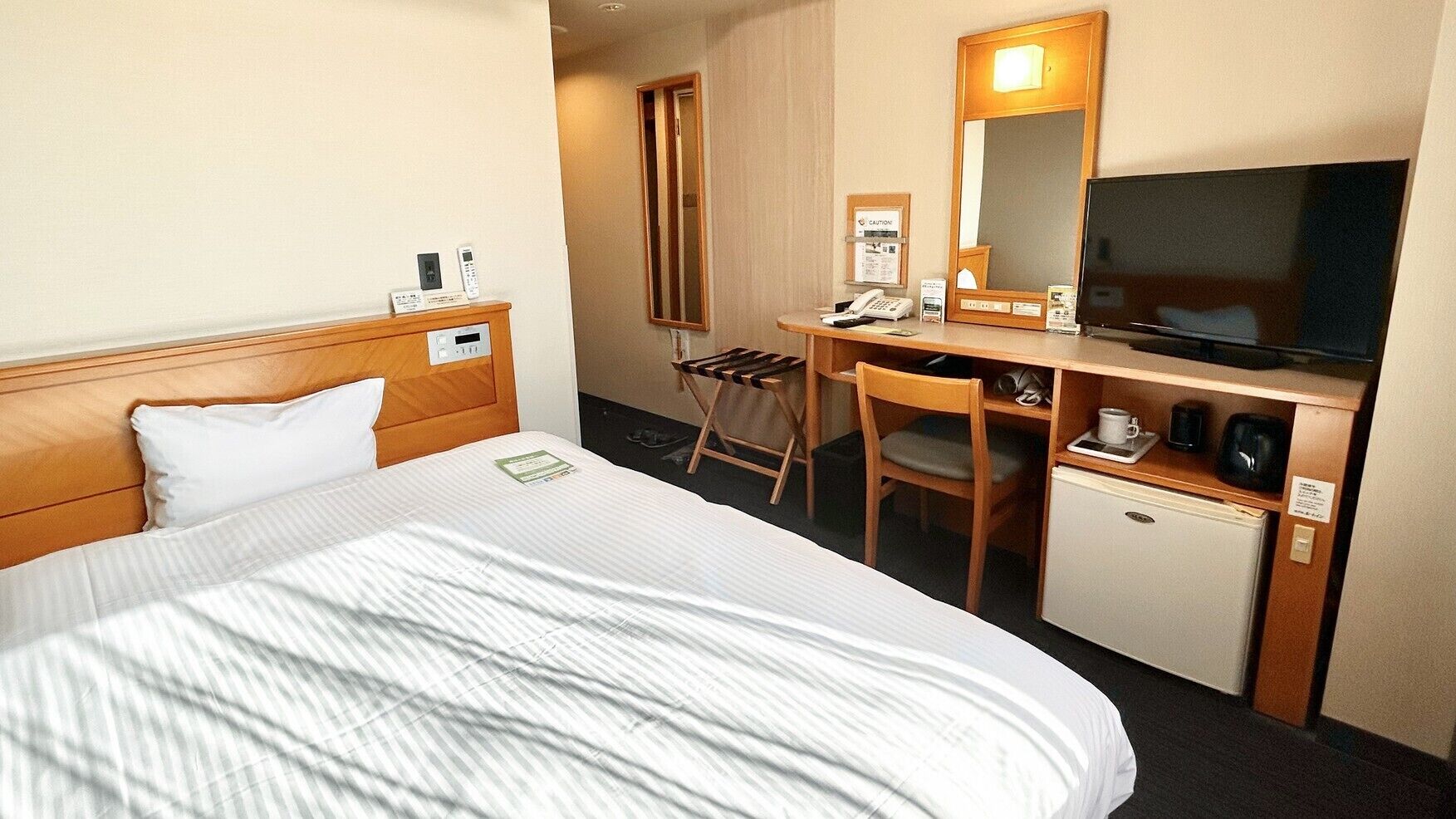 A hotel room with a bed, a desk with a chair, a television, and a mini-fridge.