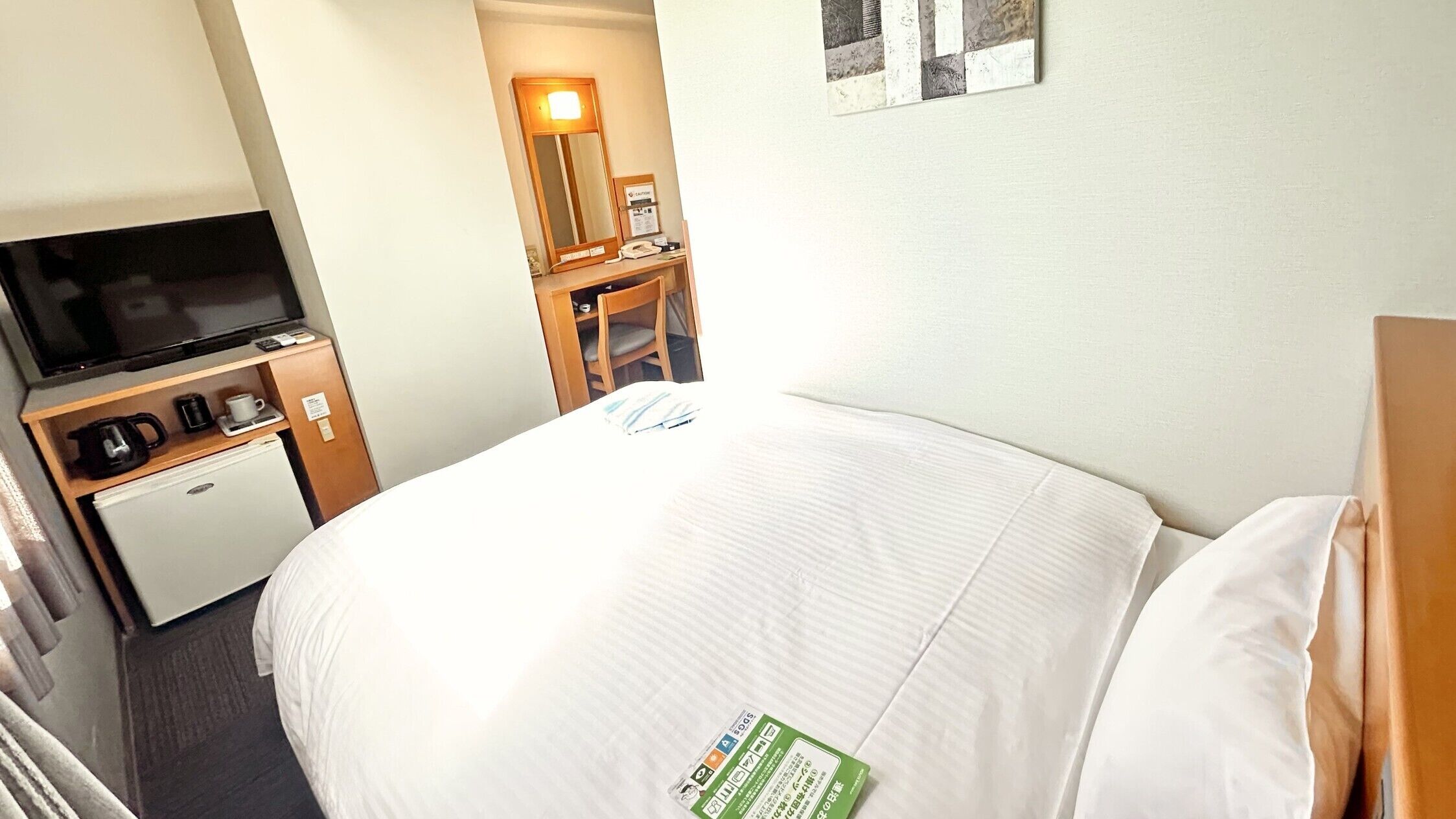 A hotel room with a bed, a television, a mini-fridge, a coffee maker, and a desk with a telephone.