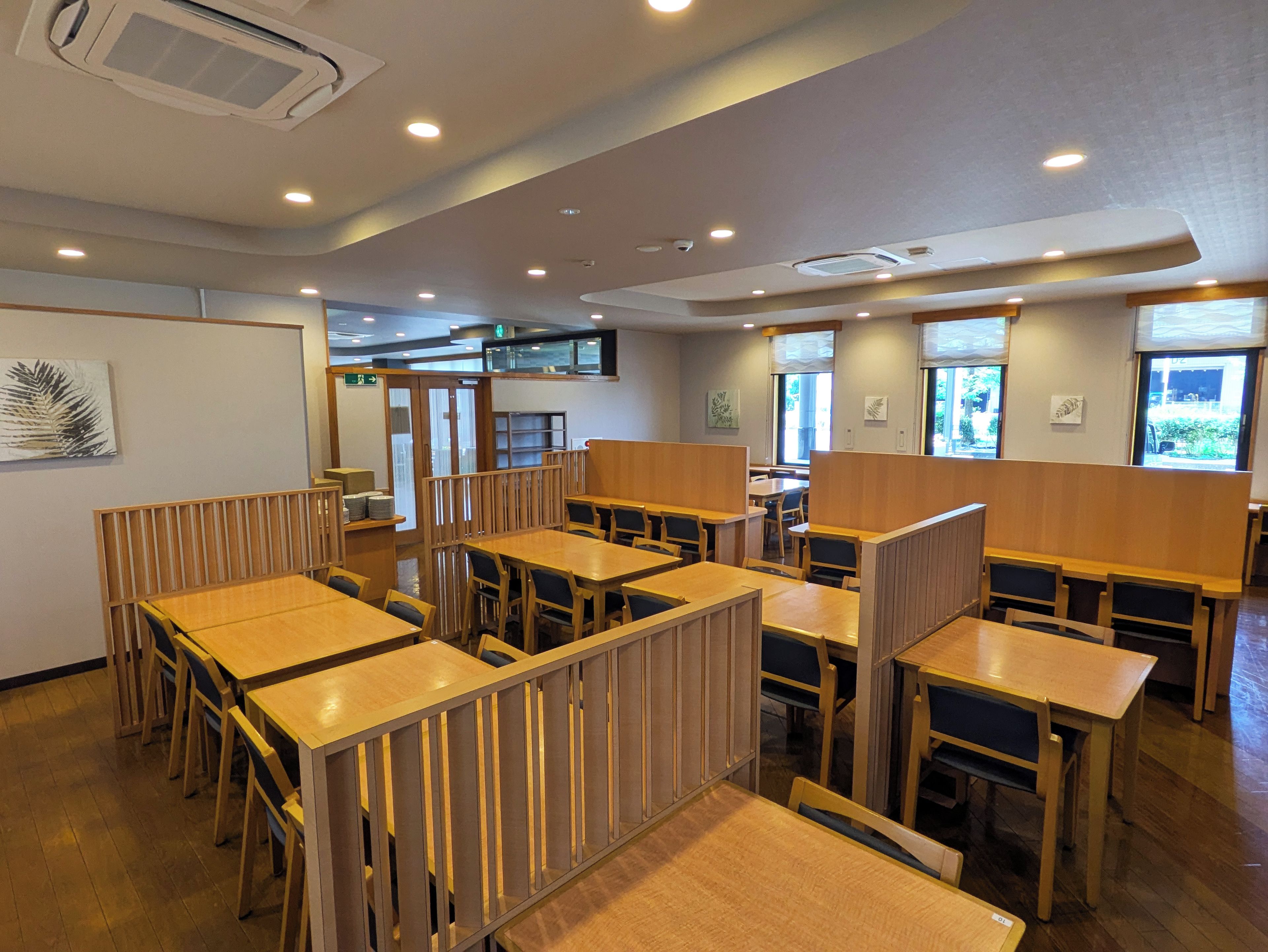 Un interior de restaurante con mesas y sillas de madera, cabinas separadas e iluminación empotrada en el techo.
