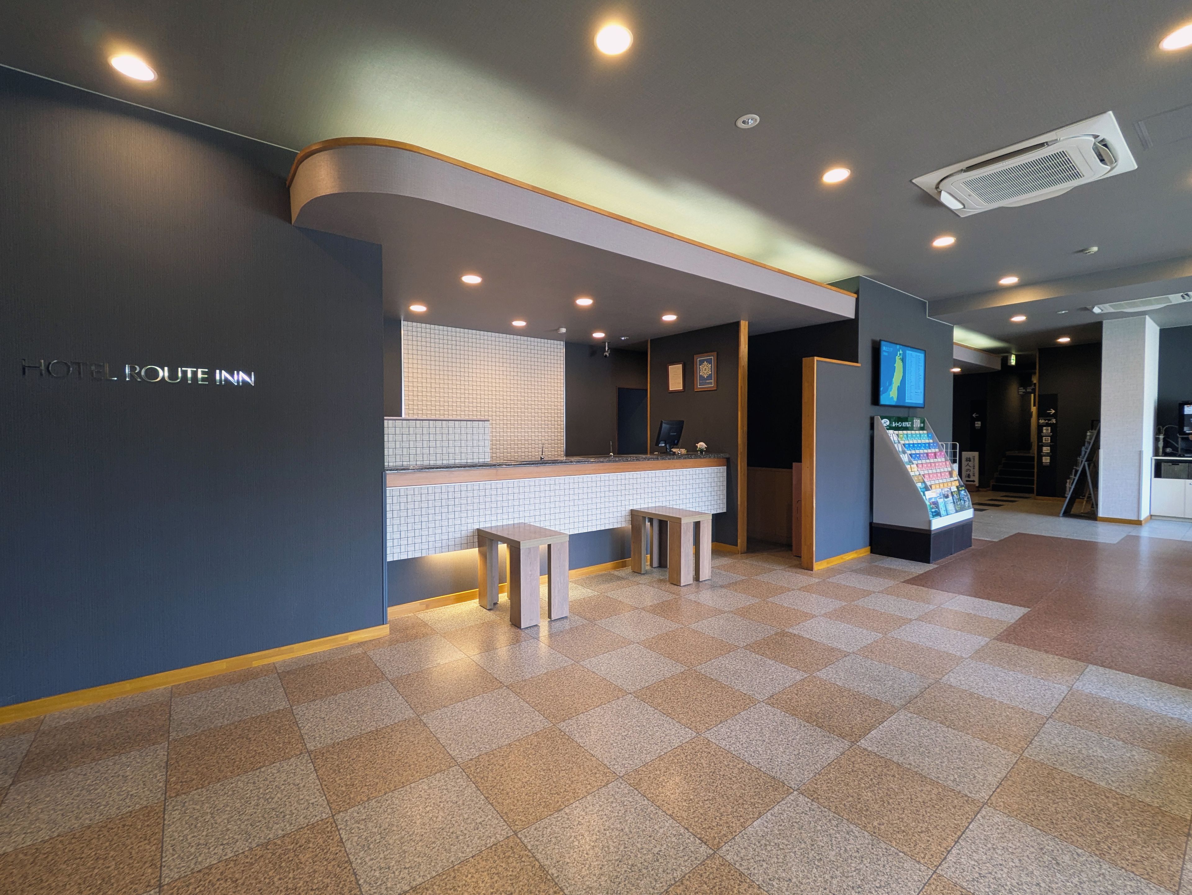 Ein Hotel-Rezeptionsbereich mit Empfangstresen, Sitzgelegenheiten und einem digitalen Bildschirm.