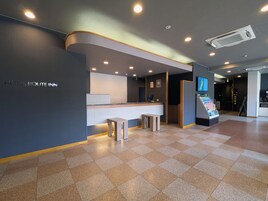 Uma área de recepção de hotel com balcão, espaço para sentar e uma tela digital.