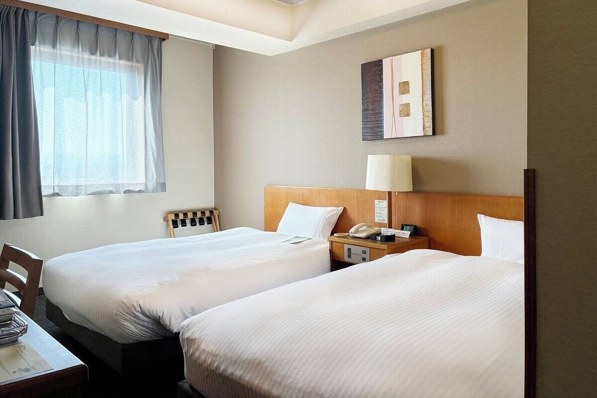 Ein Hotelzimmer mit zwei Betten, einem Schreibtisch, einer Lampe und einem Bild an der Wand.