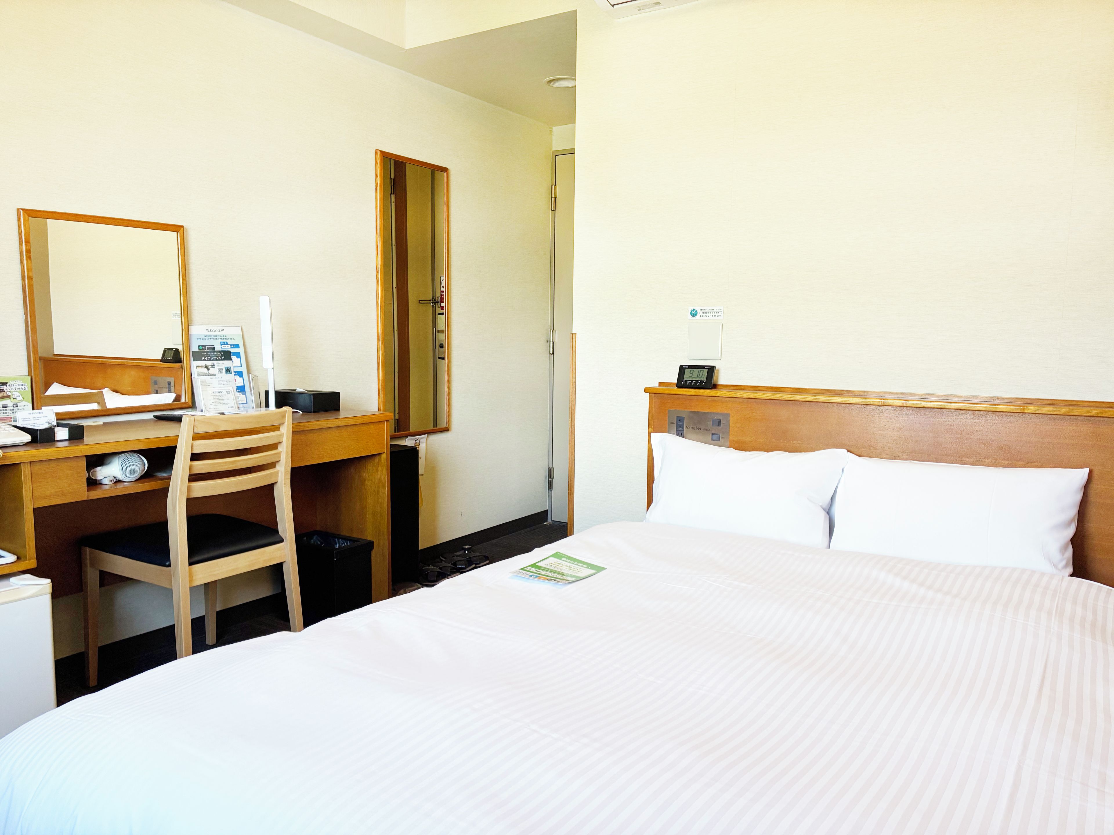 Una habitación de hotel con una cama, un escritorio, una silla, un espejo y un reloj.