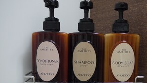 Tres botellas de productos de tocador de la marca The Amenity sobre una repisa metálica.