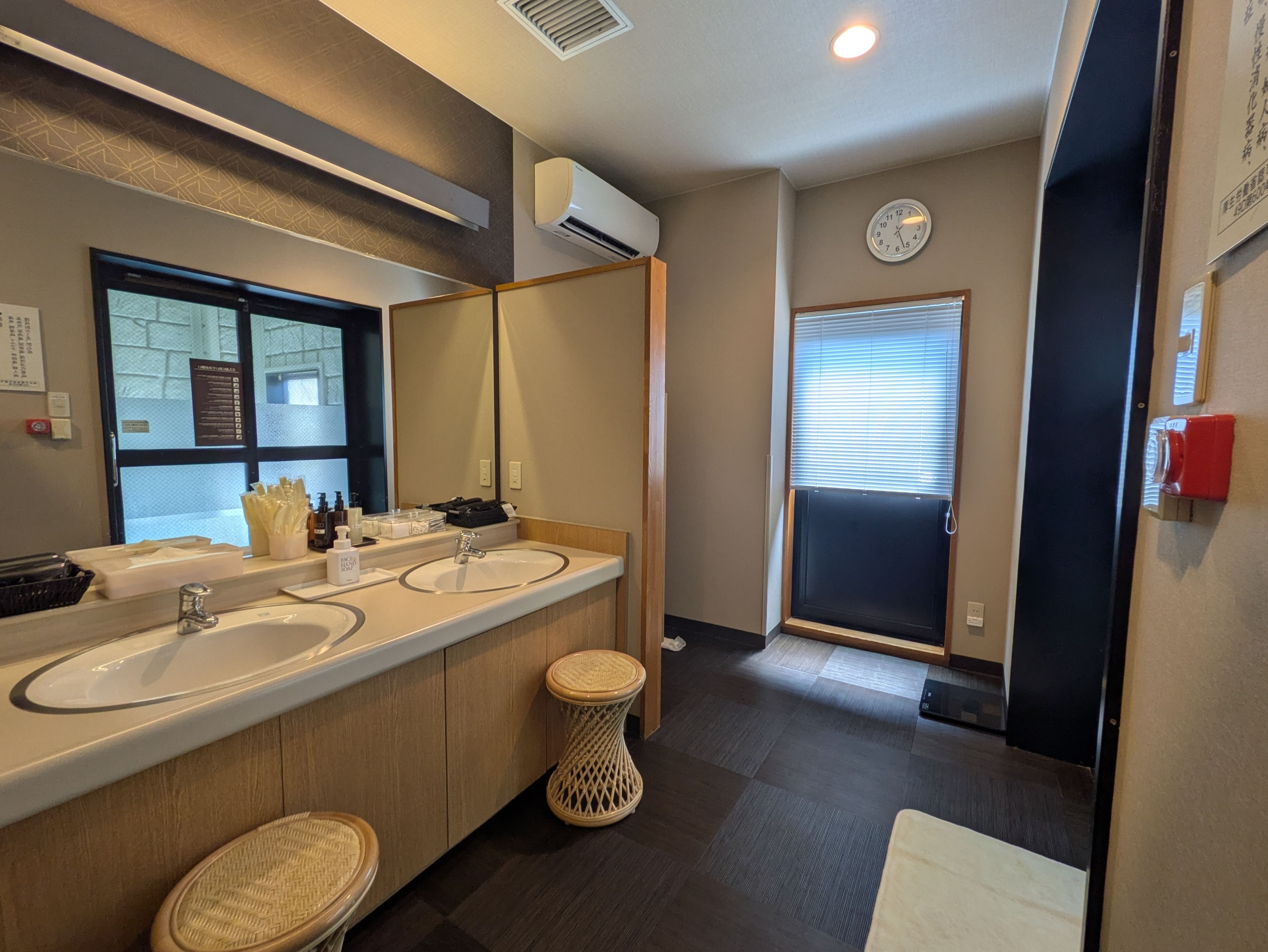 A modern bathroom with dual sinks, a large mirror, and a window with blinds.