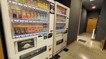 Two vending machines in a hallway with a door in the background.