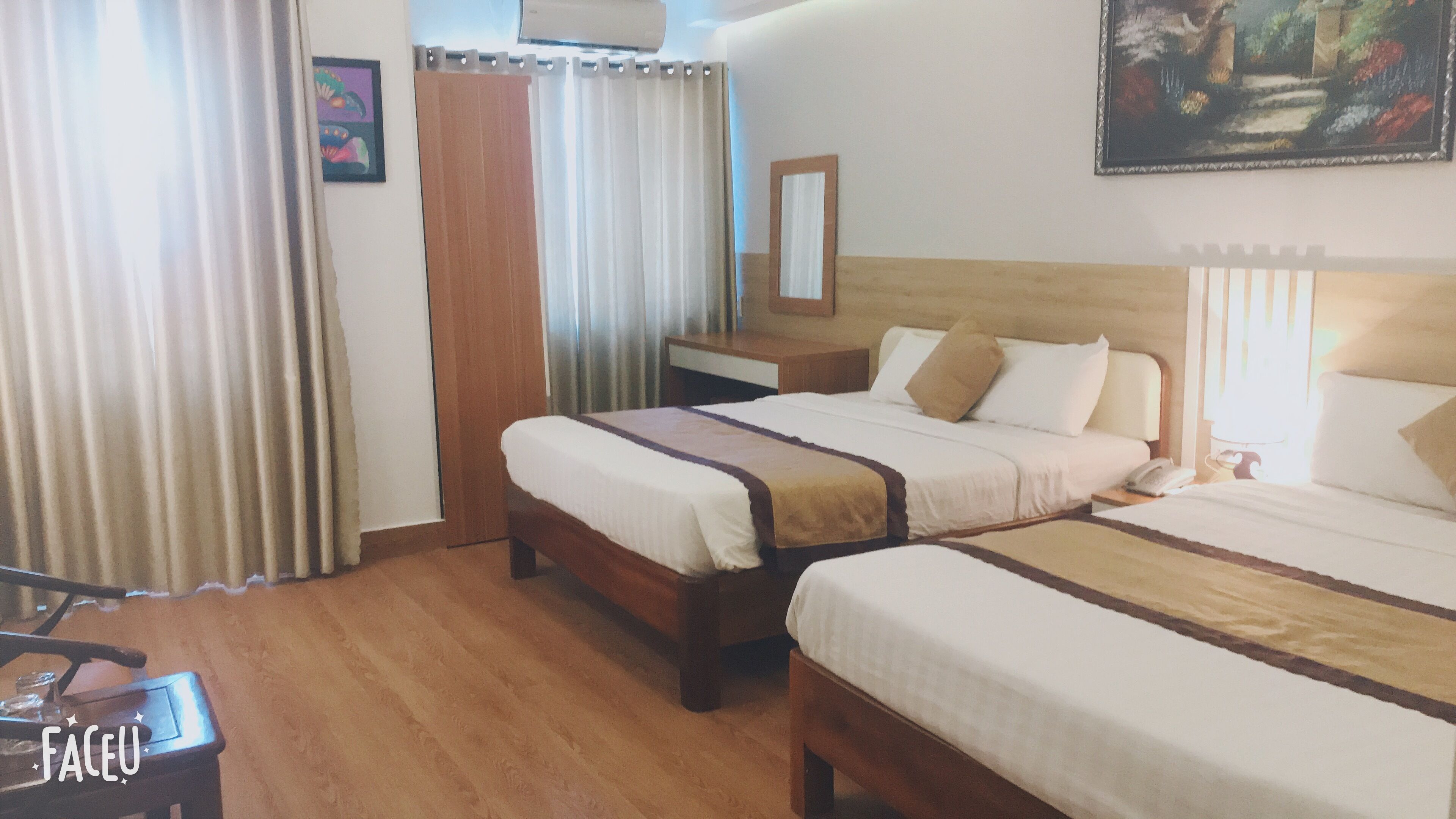 Una habitació d'hotel amb dos llits, una taula de nit de fusta, una cadira, un mirall i un quadre a la paret.