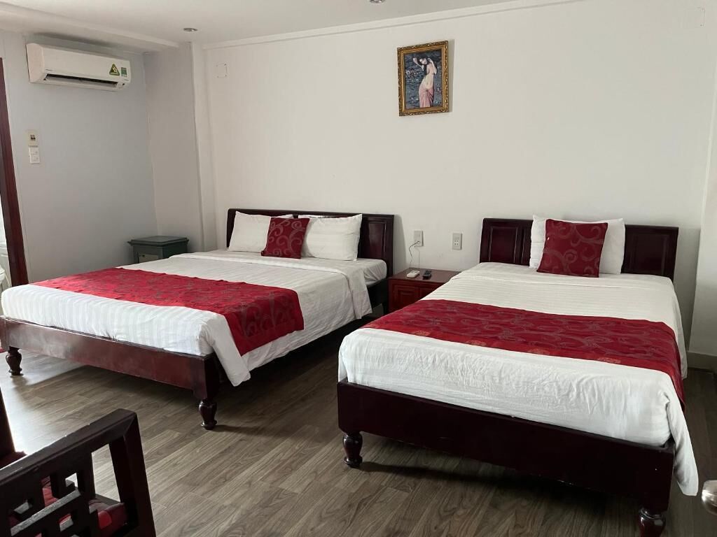 Een hotelkamer met twee bedden, elk voorzien van een rood-wit sprei, een houten vloer en een wandairconditioning.